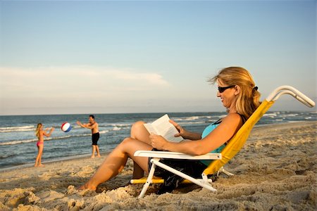 Woman at the beach reads a book while her family plays in the background by the ocean. Stock Photo - Budget Royalty-Free & Subscription, Code: 400-04168317