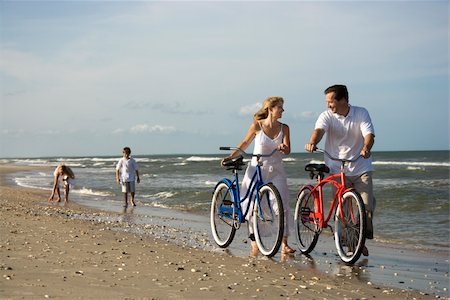 Husband and wife walk their bikes down the beach with children in the background. Horizontal shot. Stock Photo - Budget Royalty-Free & Subscription, Code: 400-04168312