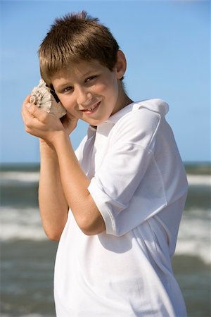 Boy listens to a shell at the beach. Vertical shot. Photographie de stock - Aubaine LD & Abonnement, Code: 400-04168788