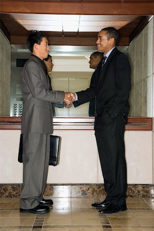 simsearch:400-04169171,k - Young adult Asian and African-American businessmen standing in an office lobby shaking hands. Foto de stock - Super Valor sin royalties y Suscripción, Código: 400-04169167