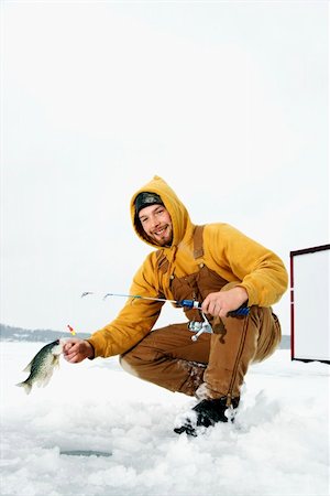 pesca en el hielo - Young man pulls a fish out of a hole in the ice. He is holding a fishing rod and wearing snow gear. Vertical shot. Foto de stock - Super Valor sin royalties y Suscripción, Código: 400-04169300