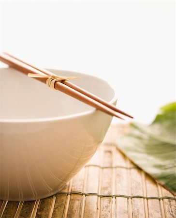 Chopsticks lying across an empty bowl on a bamboo mat, with a green leaf in the background. Vertical format. Isolated on white. Stock Photo - Budget Royalty-Free & Subscription, Code: 400-04169596