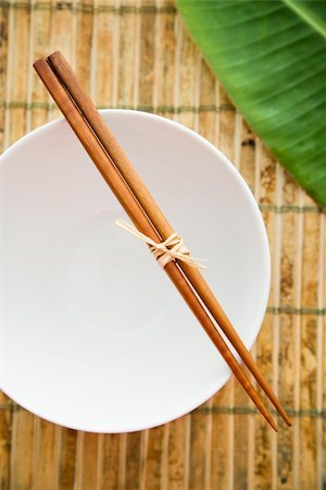 Overhead view of chopsticks lying across an empty bowl on a bamboo mat. Part of a green leaf can be seen in the background. Vertical shot. Stock Photo - Budget Royalty-Free & Subscription, Code: 400-04169597