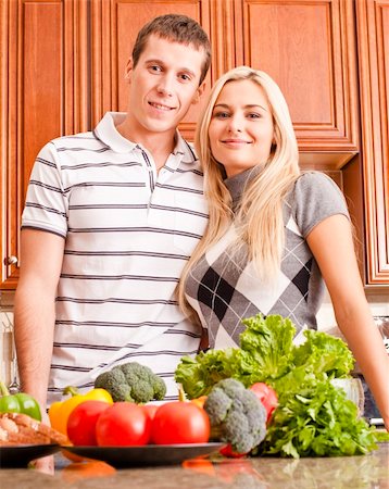 simsearch:400-04162443,k - Low angle view of young couple smiling into the camera from behind a kitchen counter. The counter is holding a selection of fresh vegetables. Vertical shot. Fotografie stock - Microstock e Abbonamento, Codice: 400-04162437