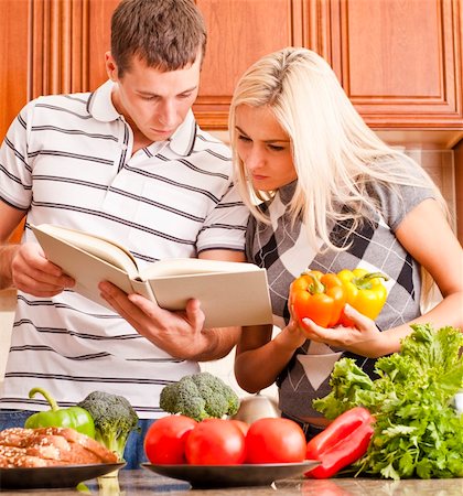 simsearch:400-04162443,k - Young couple look at a recipe book in the kitchen. The counter is full of fresh vegetables. Square shot. Fotografie stock - Microstock e Abbonamento, Codice: 400-04162444