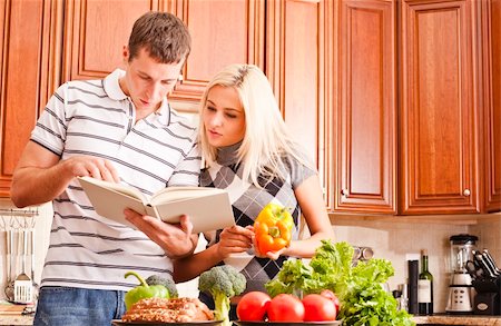 simsearch:400-04162443,k - Young couple in the kitchen read an open recipe book. The counter is full of fresh vegetables. Horizontal shot. Fotografie stock - Microstock e Abbonamento, Codice: 400-04162445