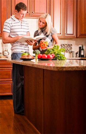 simsearch:400-04162443,k - Young couple read through a recipe book in the kitchen with a counter full of fresh vegetables. Vertical shot. Fotografie stock - Microstock e Abbonamento, Codice: 400-04162446