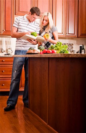 simsearch:400-04162443,k - Young couple examine a recipe book in the kitchen. The counter is full of fresh vegetables. Vertical shot. Fotografie stock - Microstock e Abbonamento, Codice: 400-04162447