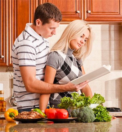 simsearch:400-04162443,k - Young couple read through a recipe book in the kitchen with a counter full of fresh vegetables. Square shot. Fotografie stock - Microstock e Abbonamento, Codice: 400-04162448