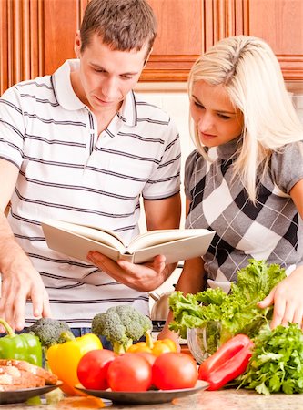 simsearch:400-04162443,k - Young couple follows a recipe book. The kitchen counter is full of fresh vegetables. Vertical shot. Fotografie stock - Microstock e Abbonamento, Codice: 400-04162443