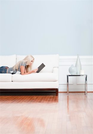 Young woman lies on a white sofa in a checkered top and blue jeans while reading a book. Vertical shot. Fotografie stock - Microstock e Abbonamento, Codice: 400-04162565