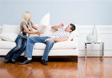 Young couple playfully have a pillow fight on a sofa.  The young man tries to avoid getting hit. Horizontal shot. Fotografie stock - Microstock e Abbonamento, Codice: 400-04162610