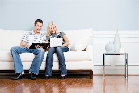 Man is reading, and woman is using a laptop, as they sit side by side on a white couch. Horizontal format. Fotografie stock - Microstock e Abbonamento, Codice: 400-04162797