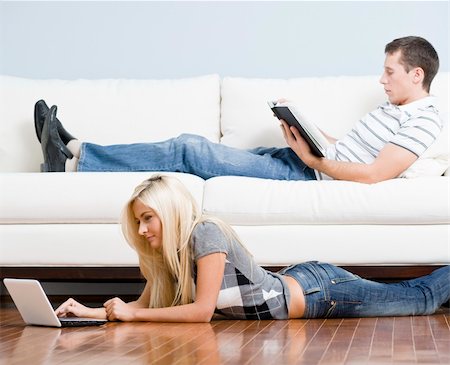 Man reads on a couch while woman stretches out on the floor with her laptop. Horizontal format. Stock Photo - Budget Royalty-Free & Subscription, Code: 400-04162814