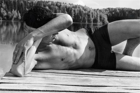 Young man in swimming trunks is lying against lake / black and white picture Stockbilder - Microstock & Abonnement, Bildnummer: 400-04178341