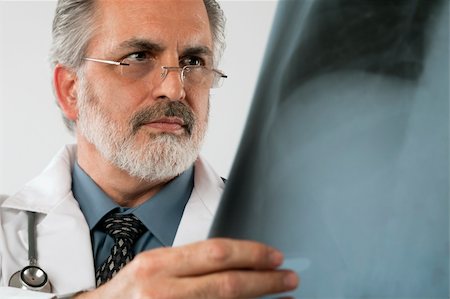 edbockstock (artist) - Cropped close-up portrait of a doctor wearing eyeglasses and a white lab coat and looking intently at an x-ray. Horizontal shot. Isolated on white. Photographie de stock - Aubaine LD & Abonnement, Code: 400-04172666