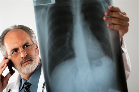 edbockstock (artist) - Selective focus image of a doctor wearing glasses and a white lab coat and looking intently at an x-ray while using his cell phone. Horizontal shot. Photographie de stock - Aubaine LD & Abonnement, Code: 400-04172667