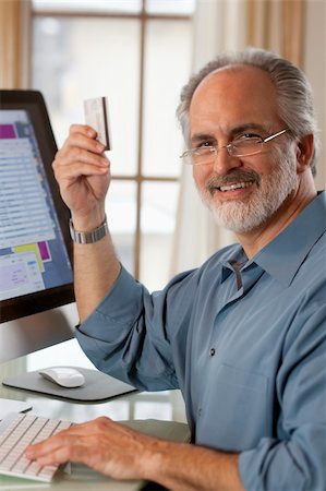 senior online shopping - A businessman sitting in front of a computer monitor and holding up a credit card.  He is smiling at the camera. Vertical shot. Stock Photo - Budget Royalty-Free & Subscription, Code: 400-04172660