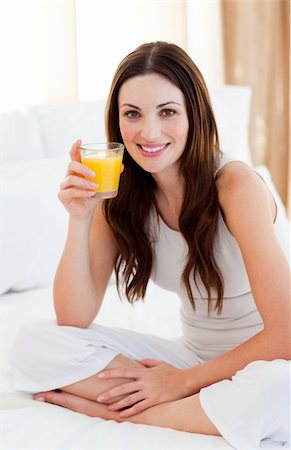 simsearch:400-03998265,k - Brunette woman drinking orange juice sitting on bed at home Fotografie stock - Microstock e Abbonamento, Codice: 400-04188982