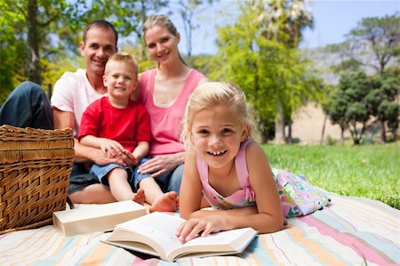 simsearch:400-04195786,k - Cute little girl reading lying on the grass while having a picnic with her family in a park Foto de stock - Royalty-Free Super Valor e Assinatura, Número: 400-04195784