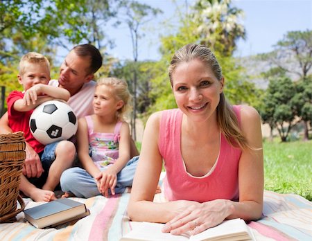 simsearch:400-04195786,k - Smiling woman reading at a picnic with her family in the background Foto de stock - Royalty-Free Super Valor e Assinatura, Número: 400-04195791