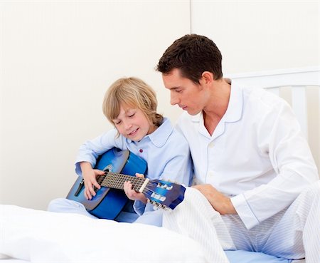 father son indoors - Adorable little boy playing guitar with his father in the bedroom Photographie de stock - Aubaine LD & Abonnement, Code: 400-04195898