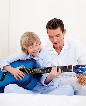 father son indoors - Smiling little boy playing guitar with his father in the bedroom Photographie de stock - Aubaine LD & Abonnement, Code: 400-04195891