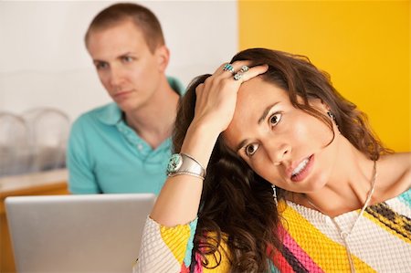 simsearch:400-04717564,k - Image of a woman in the foreground with a frustrated expression while in the background a man is using a laptop. Horizontal shot. Stockbilder - Microstock & Abonnement, Bildnummer: 400-04196324