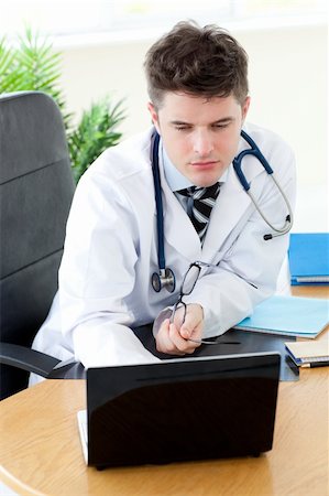 simsearch:400-04191693,k - Confident male doctor using a laptop sitting at his desk in a practice Stock Photo - Budget Royalty-Free & Subscription, Code: 400-04191695