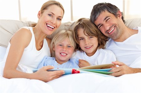 simsearch:400-04192370,k - Smiling family reading a book  lying in bed Fotografie stock - Microstock e Abbonamento, Codice: 400-04193064
