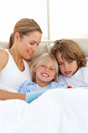 simsearch:400-04192370,k - Pretty mother and her children reading book lying in bed Fotografie stock - Microstock e Abbonamento, Codice: 400-04193076