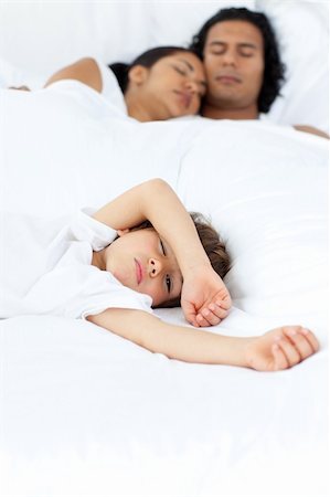 simsearch:400-04192370,k - Little boy relaxing on the bed with his parents sleeping in the background Fotografie stock - Microstock e Abbonamento, Codice: 400-04193379