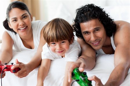 Parents and their little boy playing video games lying on the bed Stock Photo - Budget Royalty-Free & Subscription, Code: 400-04193392