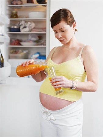 simsearch:400-04416091,k - italian 6 months pregnant woman standing near refrigerator and drinking orange juice. Three quarter length, vertical shape Fotografie stock - Microstock e Abbonamento, Codice: 400-04204145