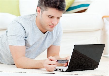 pictures of man lying on money - Concentrated man holding a credit card looking at a laptop lying on the floor in the living room Stock Photo - Budget Royalty-Free & Subscription, Code: 400-04204851