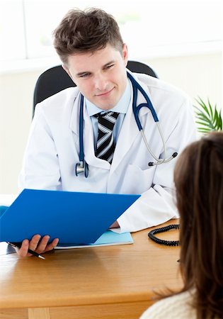 simsearch:400-04281577,k - Smiling young doctor holding a folder talking with his brunette patient Photographie de stock - Aubaine LD & Abonnement, Code: 400-04205550