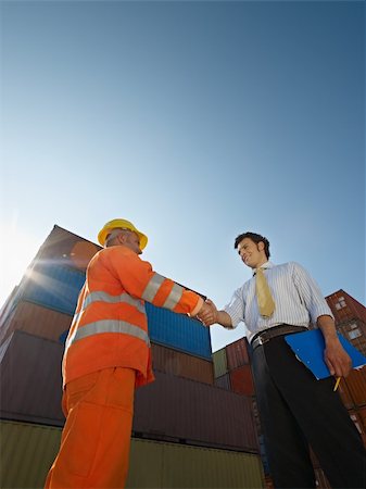 people, shake hand, industry - Mid adult businessman holding clipboard and shaking hands to manual worker near cargo containers. Vertical shape, low angle view. Copy space Stock Photo - Budget Royalty-Free & Subscription, Code: 400-04205714