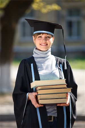 school girl holding pile of books - Portrait of young female graduate with stack of books, in sunlight, with blurred college building in the background Stock Photo - Budget Royalty-Free & Subscription, Code: 400-04205766