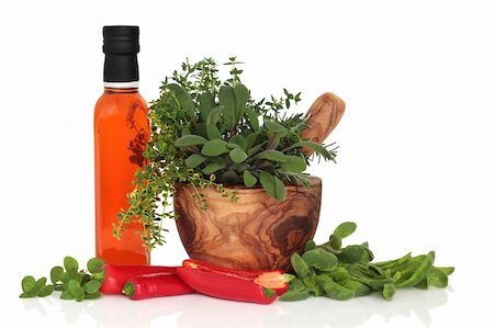 Olive chilli oil, chillies, and herb leaf sprigs of rosemary, purple and variegated sage, thyme and oregano in an olive wood mortar with pestle, isolated over white background. Stockbilder - Microstock & Abonnement, Bildnummer: 400-04205906