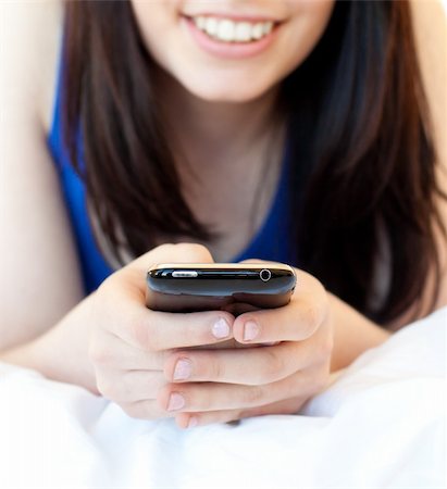 Close-up of a brunette teenager texting while lying on her bed against white background Stock Photo - Budget Royalty-Free & Subscription, Code: 400-04206759