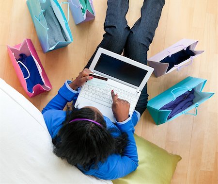 Pretty afro-american teenager using a laptop sitting between shopping bags on the floor in the living room Stock Photo - Budget Royalty-Free & Subscription, Code: 400-04206774