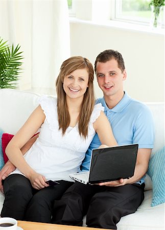 simsearch:400-05741872,k - Enthusiastic couple using laptop smiling at the camera sitting on a sofa at home Stock Photo - Budget Royalty-Free & Subscription, Code: 400-04208852