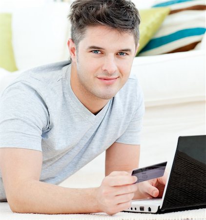 simsearch:400-05209351,k - Charming young man holding a card smiling at the camera lying on the floor at home Stock Photo - Budget Royalty-Free & Subscription, Code: 400-04209846