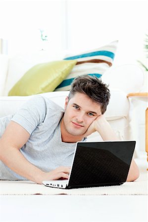 simsearch:400-05209351,k - Charismatic young man using his laptop lying on the floor at home looking at the camera Stock Photo - Budget Royalty-Free & Subscription, Code: 400-04209847