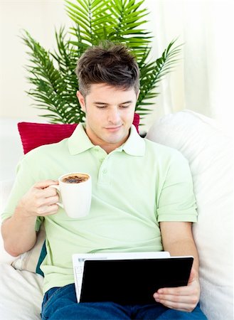 simsearch:400-04212835,k - Concentrated young man using his laptop drinking coffee on the sofa Photographie de stock - Aubaine LD & Abonnement, Code: 400-04209843