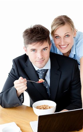 Enamored couple of businesspeople smiling at camera eating cereals against white background Stock Photo - Budget Royalty-Free & Subscription, Code: 400-04209950