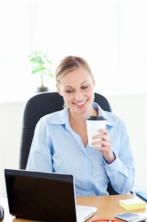 simsearch:400-04187842,k - Smiling businesswoman holding a coffee while using a laptop at work Stock Photo - Budget Royalty-Free & Subscription, Code: 400-04202059