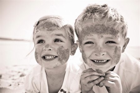 simsearch:400-04218582,k - Brother and sister smile at the camera, brightly lit, on the beach, faces covered in sand. Stockbilder - Microstock & Abonnement, Bildnummer: 400-04214060