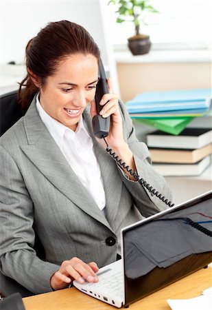 simsearch:400-04341796,k - Busy businesswoman talking on phone and using her laptop sitting at her desk in her office Stockbilder - Microstock & Abonnement, Bildnummer: 400-04217178