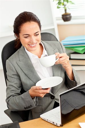 simsearch:400-04187842,k - Smiling businesswoman holding a coffee while using a laptop at work in her office Stock Photo - Budget Royalty-Free & Subscription, Code: 400-04217181